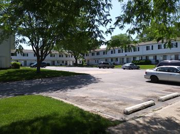 A parking lot with a tree and a car in front of a building.